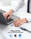 Person using a laptop with a USB device, connected to a hub, on a desk.