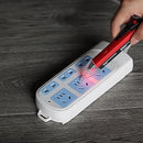 Mr. Pen - A hand holds a red and black electronic plug tester over a white power strip with blue outlets, placed on a gray wood-textured floor. The tester illuminates the socket connections with a red light.