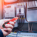 Mr. Pen - A close-up of a hand holding a red and black electrical test tool in front of an electrical meter and circuit breaker panel with copper wires.