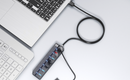 A black multi-port USB power strip with switches and indicator lights, shown plugged into a laptop on a clean white surface.