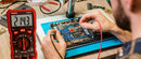 Person working on a circuit board with a multimeter displaying 214.3 volts.