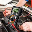 ANENG Digital multimeter being used to test a car battery with a person's hands visible.
